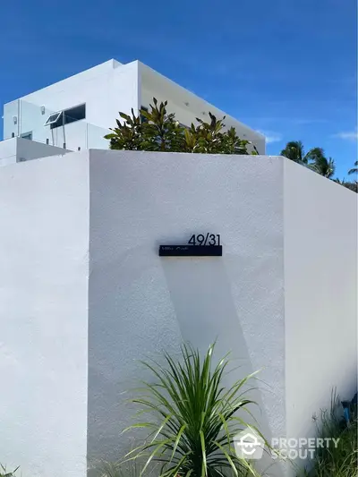 Modern white villa exterior with lush greenery and clear blue sky