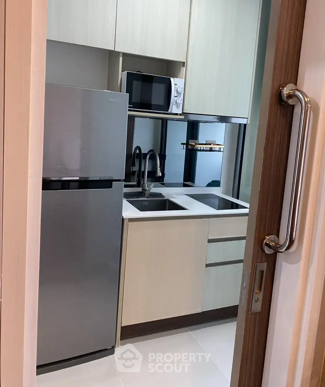 Modern compact kitchen with stainless steel fridge and microwave, sleek cabinetry, and dual sink.