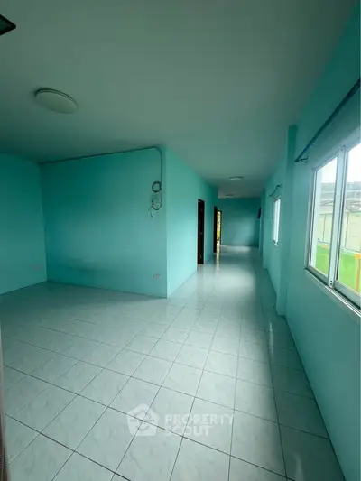Spacious empty room with turquoise walls and large windows, perfect for customization.