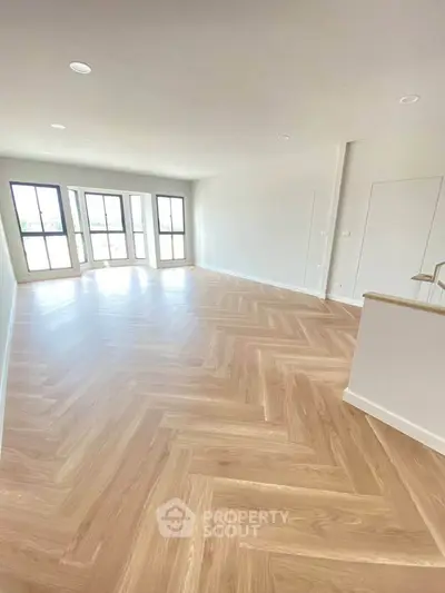 Spacious modern living room with elegant herringbone wood flooring and large windows for natural light.