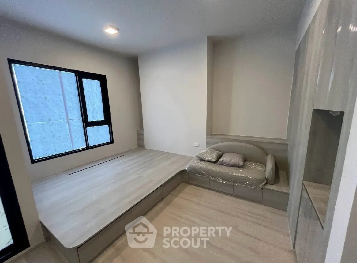 Modern bedroom with built-in platform bed and cozy seating area, featuring sleek design and ample natural light.