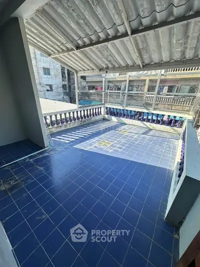 Spacious tiled balcony with partial roof cover and urban view, ideal for outdoor relaxation.