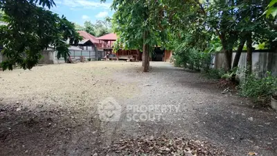 Spacious backyard with lush trees and traditional house, perfect for outdoor activities and relaxation.