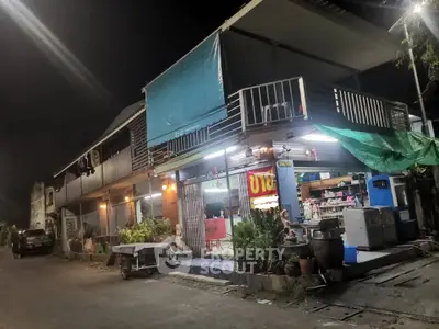 Charming two-story building with vibrant street view and lush greenery at night.