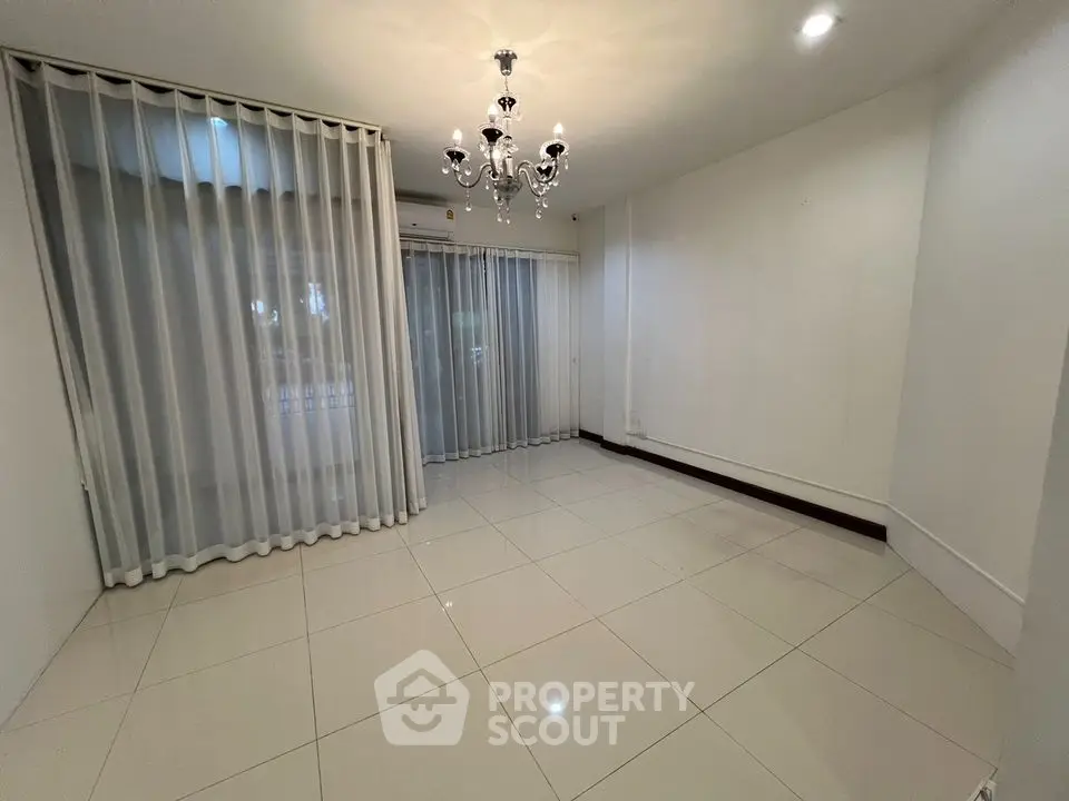 Spacious empty room with elegant chandelier and large windows with sheer curtains.