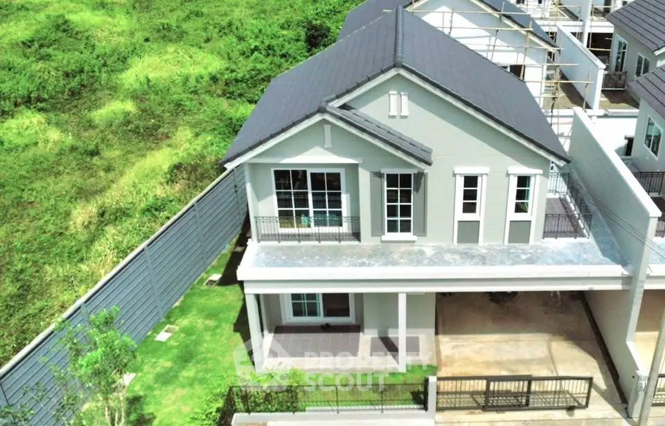 Modern two-story house with spacious balcony and lush green surroundings.