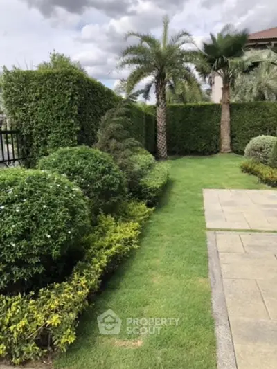 Lush green garden with palm trees and manicured hedges in a serene residential setting.