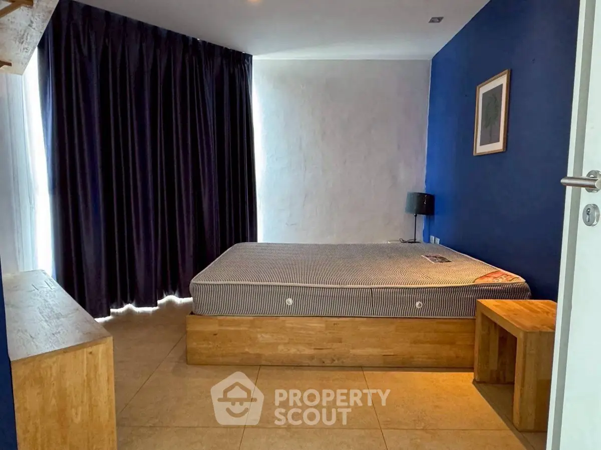 Modern minimalist bedroom with blue accent wall and wooden furniture.