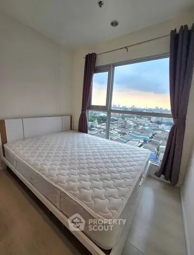 Cozy bedroom with large window offering stunning city views, featuring a comfortable mattress and elegant curtains.