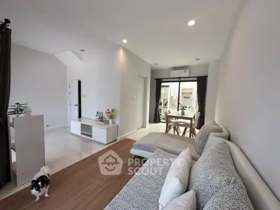 Modern living room with stylish furniture and open layout, leading to a bright dining area with large windows.