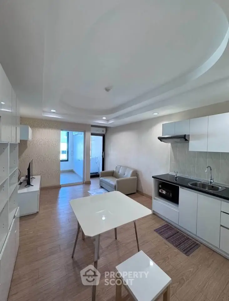 Modern open-plan living room with kitchen, featuring sleek white cabinetry and cozy seating area.