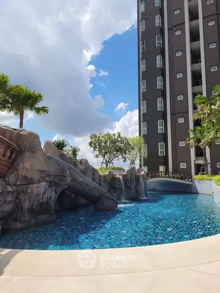 Luxurious high-rise building with stunning pool and lush landscaping under a bright blue sky.