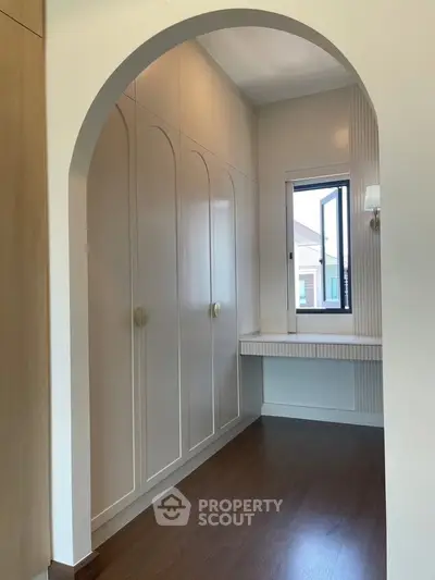 Elegant walk-in closet with arched entry and natural light, featuring built-in storage and a stylish vanity area.