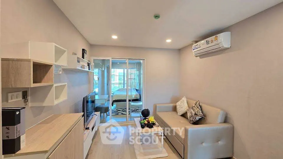 Modern living room with sleek furniture and air conditioning, featuring a view into a cozy bedroom.
