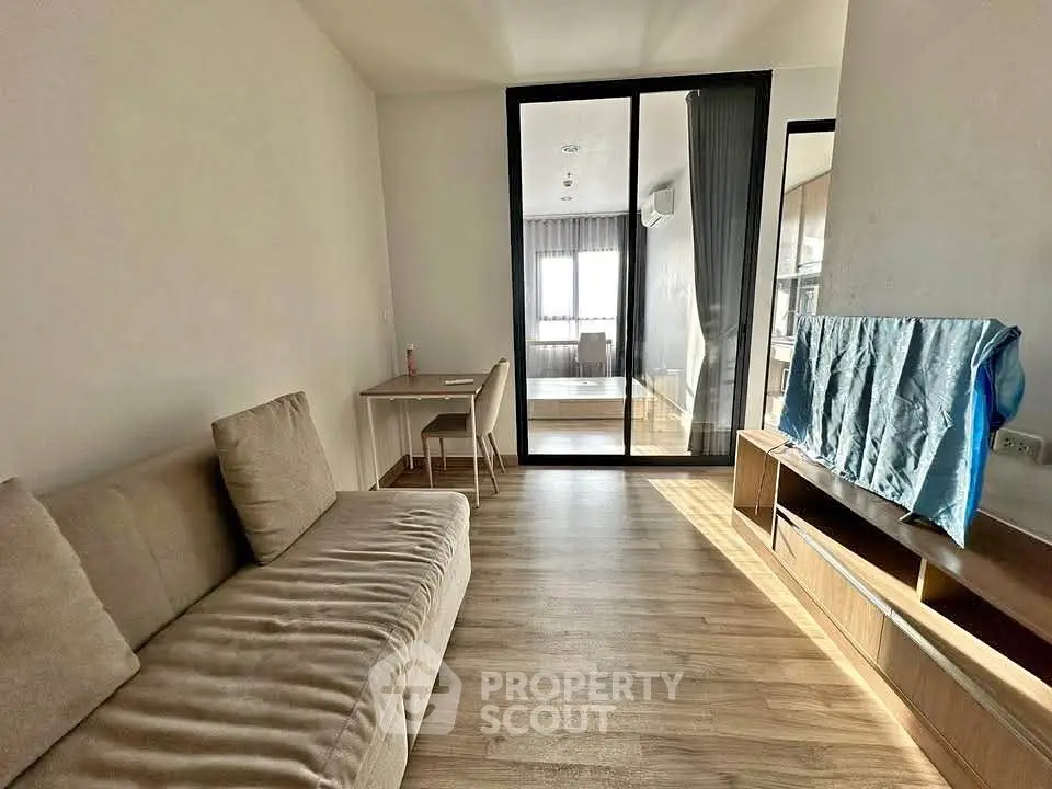 Modern living room with wooden flooring and sliding glass doors leading to a bright bedroom.