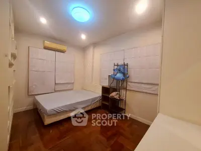 Cozy bedroom with wooden flooring and soft lighting, featuring a neatly made bed and air conditioning.