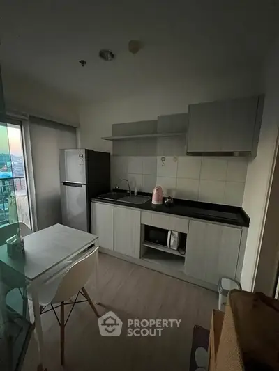 Modern compact kitchen with sleek cabinetry and dining area, featuring a fridge and microwave.