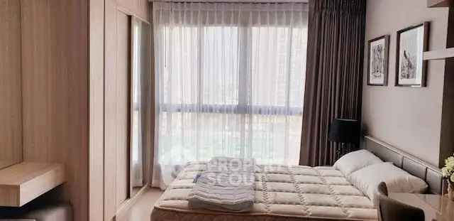 Modern bedroom with large window and stylish decor in urban apartment.