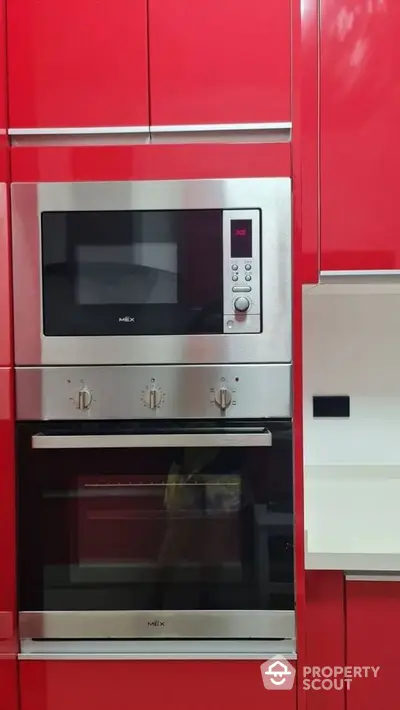 Modern kitchen with sleek red cabinets and built-in stainless steel oven and microwave.