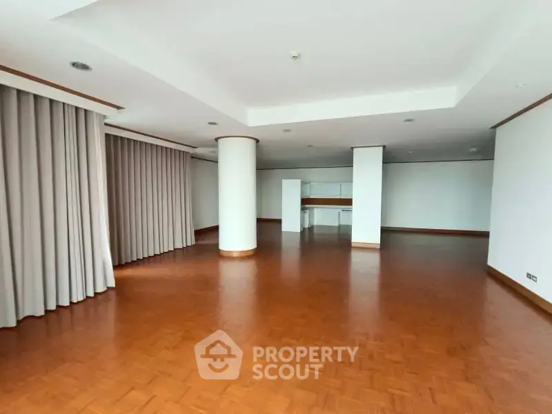 Spacious open-plan living area with wooden flooring and large windows.