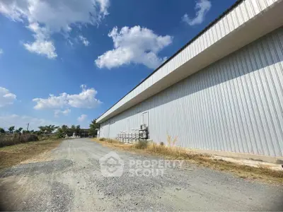 Expansive industrial warehouse exterior with clear blue sky and gravel driveway.