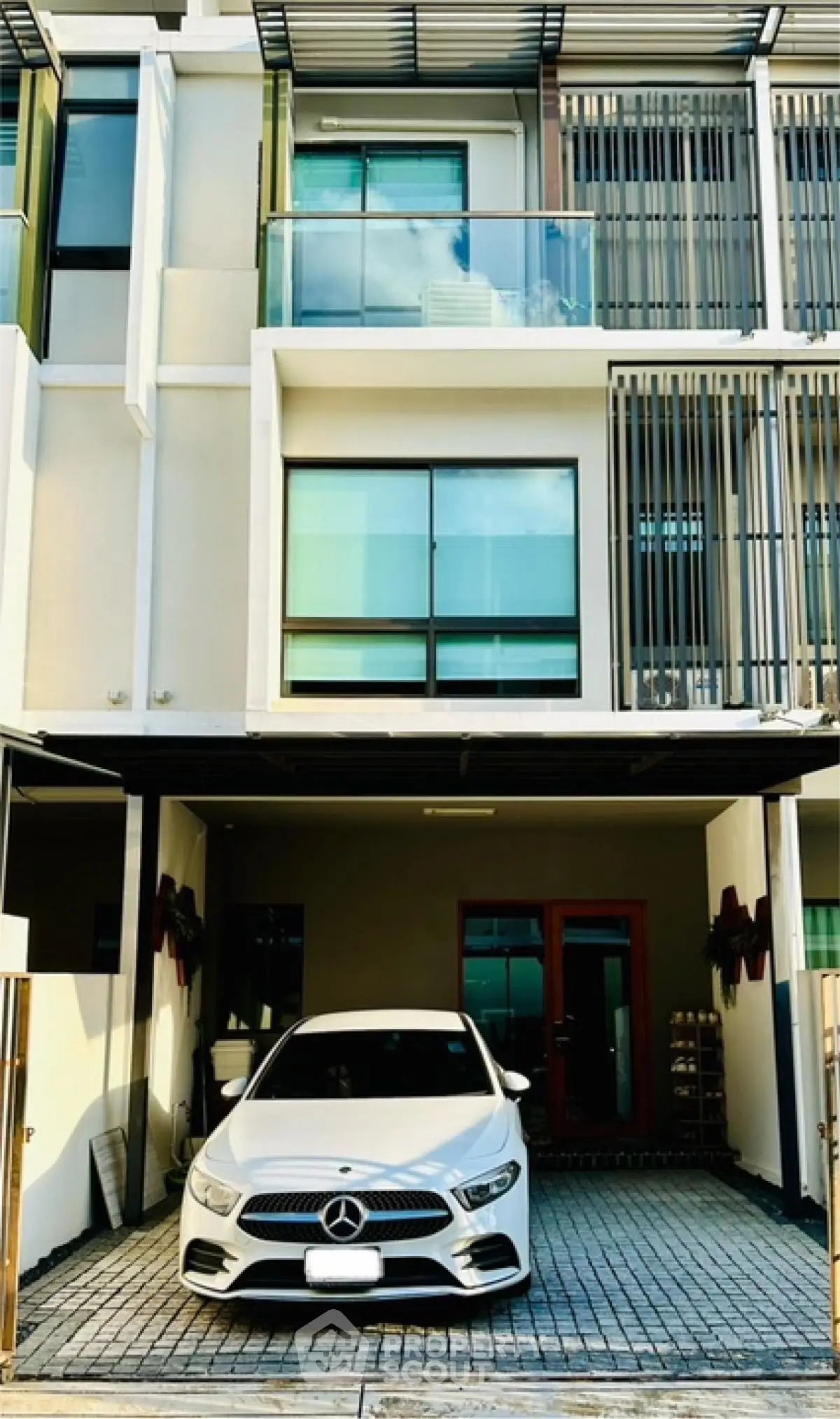 Modern townhouse with sleek facade and carport featuring luxury vehicle.