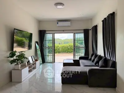 Modern living room with sleek black sofa, large TV, and scenic garden view.