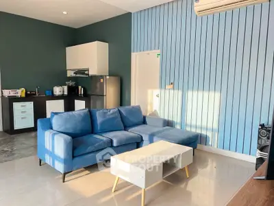 Modern living room with blue sofa and open kitchen layout, featuring sleek appliances and stylish decor.
