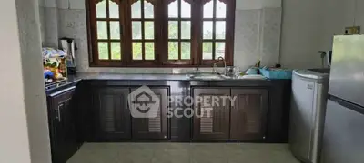 Charming kitchen with wooden cabinets and large window offering lush green views.