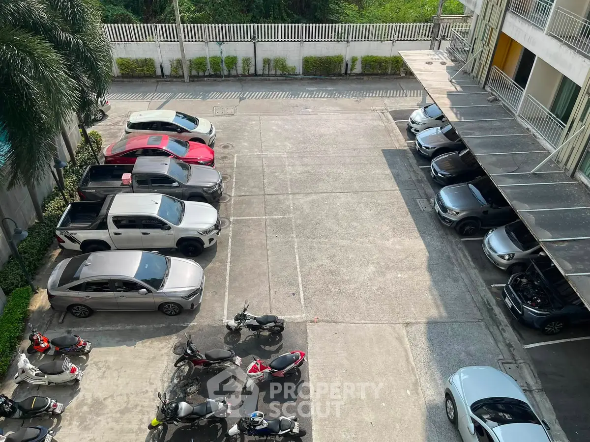 Spacious parking area with cars and motorcycles in a residential building complex.