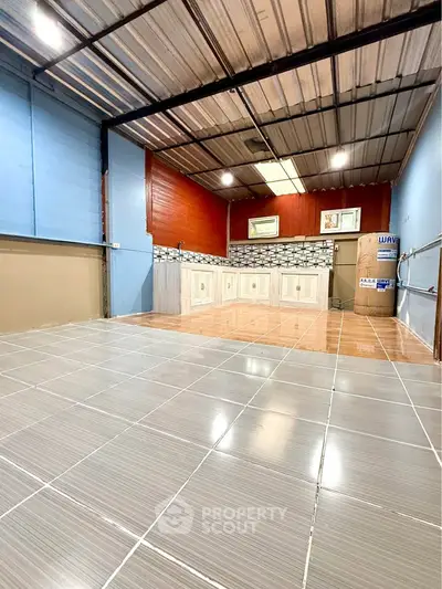 Spacious tiled room with modern kitchen area and high ceiling, perfect for versatile living space.