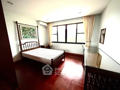 Spacious bedroom with wooden flooring and large windows in a modern apartment.