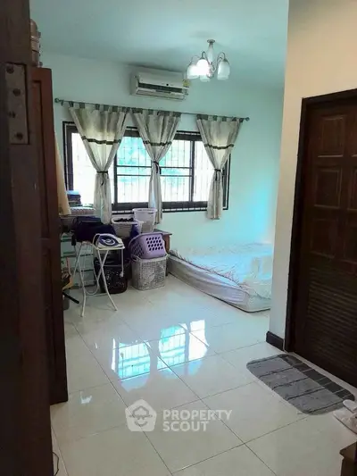 Cozy bedroom with natural light and tiled flooring, featuring a window air conditioner and minimalist decor.
