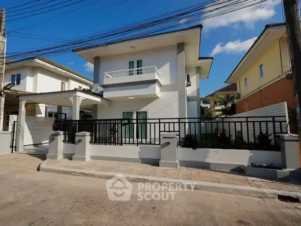 Modern two-story house with balcony and gated entrance in a suburban neighborhood.