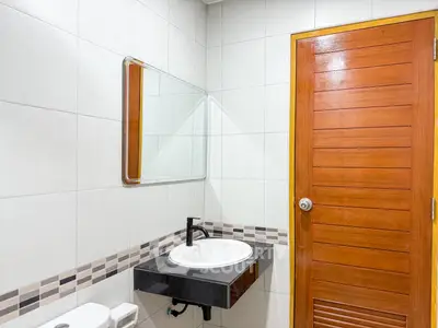 Modern bathroom with sleek sink and wooden door, featuring stylish tile accents.