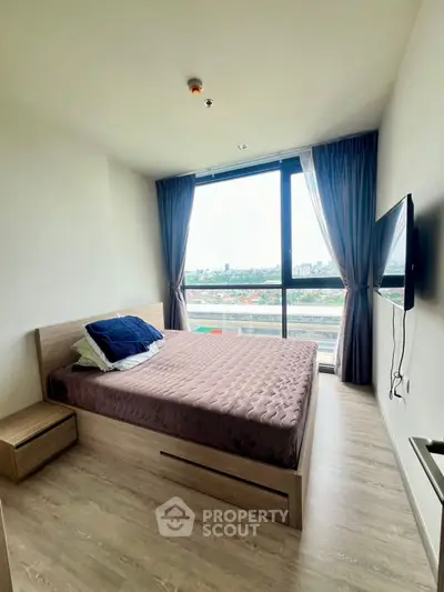 Modern bedroom with large window and city view, featuring a mounted TV and minimalist decor.