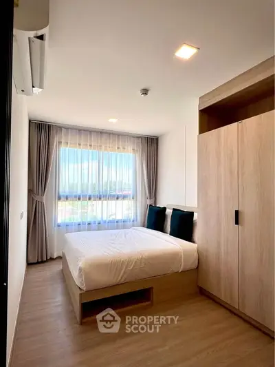 Modern bedroom with large window and wooden wardrobe, featuring cozy bedding and natural light.