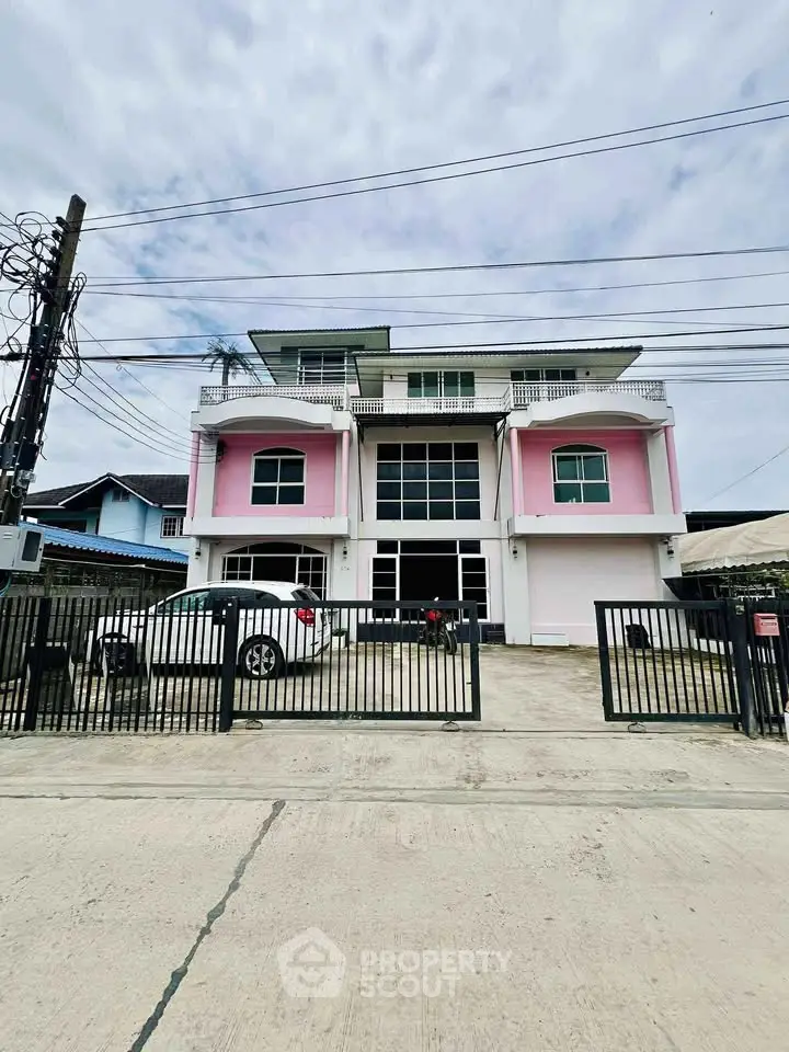 Charming three-story building with pink accents and gated parking area.
