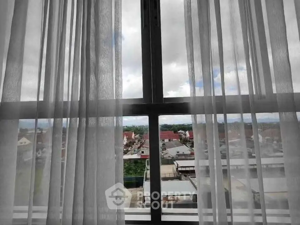 Stunning urban view through sheer curtains from a high-rise window, showcasing cityscape and sky.