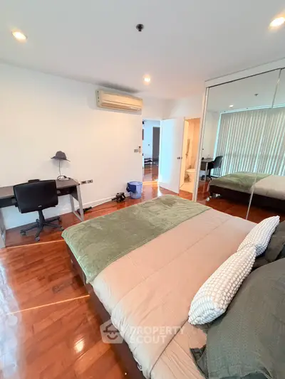 Spacious bedroom with modern decor and mirrored closet doors, featuring hardwood floors and ample natural light.