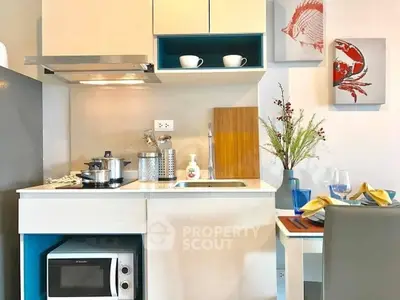 Bright and modern kitchenette with sleek white countertops, blue cabinets, stainless steel appliances, and artistic wall decor, perfect for urban living.