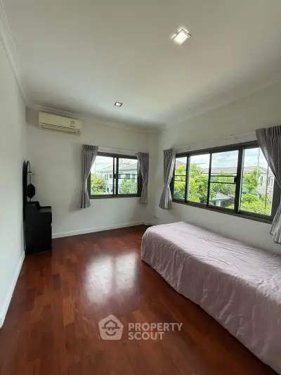 Spacious bedroom with large windows and wooden flooring, offering a serene view.