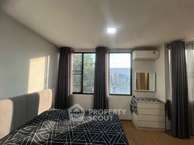 Modern bedroom with large windows and stylish decor, featuring a comfortable bed and sleek dresser.