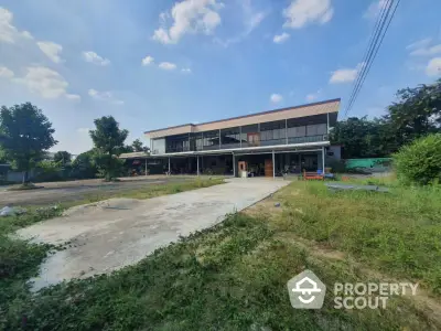 Spacious modern building with expansive driveway and lush greenery under a clear blue sky.