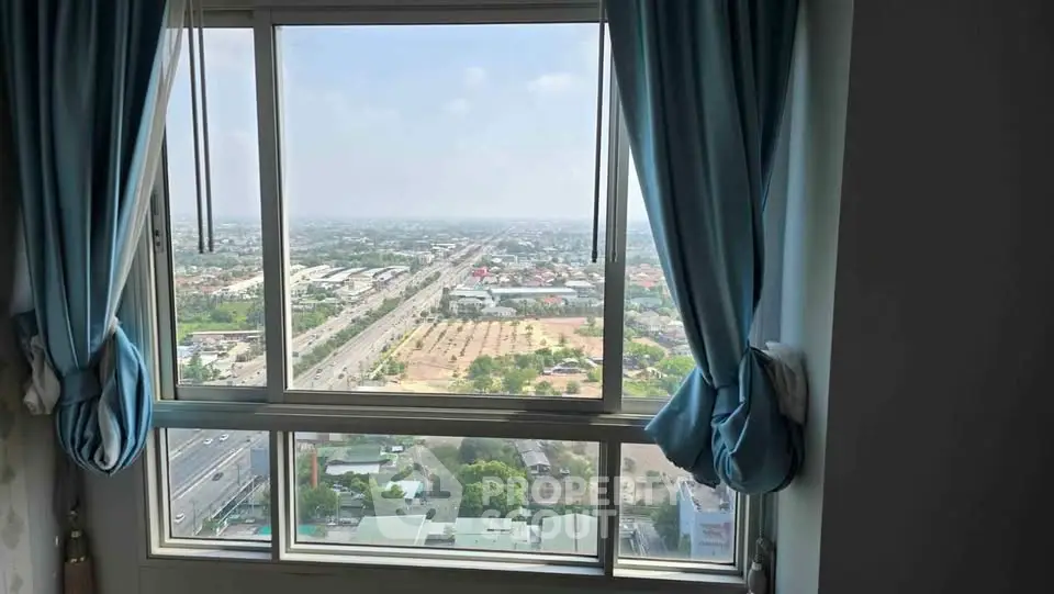 Stunning high-rise window view with blue curtains overlooking cityscape and highway.