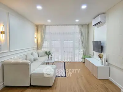 Elegant living room with modern decor, featuring a plush sofa, wall-mounted TV, and large windows.