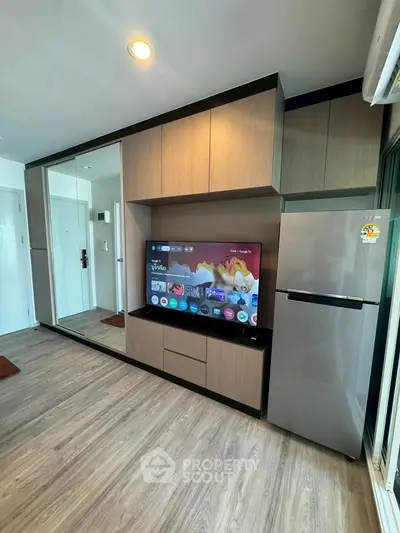 Modern living room with sleek cabinetry and large TV, featuring a stylish fridge and wood flooring.