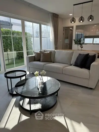 Modern living room with elegant sofa and glass coffee table, large windows offering garden view.