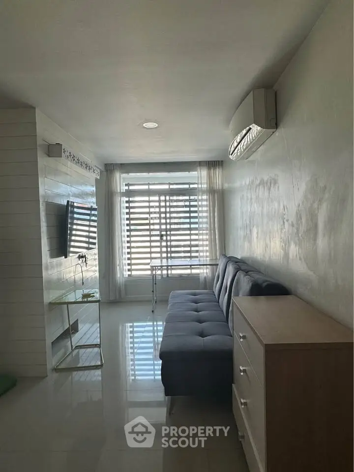 Modern living room with sleek furniture and natural light, featuring a wall-mounted TV and air conditioning.