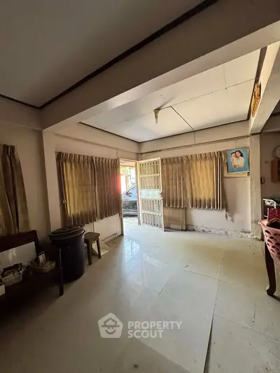 Spacious living room with natural light and tiled flooring, featuring large windows and open layout.